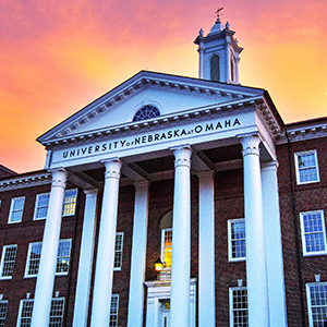 Arts and Sciences Hall building with large white columns in front of a pink and orange sunset.